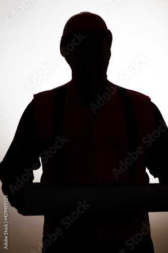 silhouette of builder contractor in hard hat looking with a scroll of paper plans on white isolated background, building industry concept