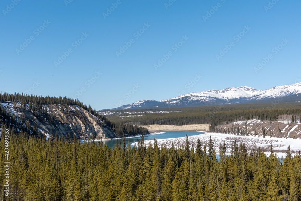 Winding Yukon River outside of Whitehorse in spring time with wonderful scenic view of the wilderness surrounding snow capped mountain peaks in the background. Desktop wallpaper, tourism, visit. 