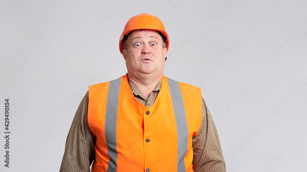 fat construction worker in funny confusion in helmet on grey background, bulder does not understand with humorous face expression fat construction worker in funny confusion in helmet on grey background, bulder does not understand with humorous face expression