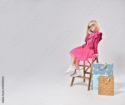 Fashionable girl child talking on the phone and sitting next to shopping bags