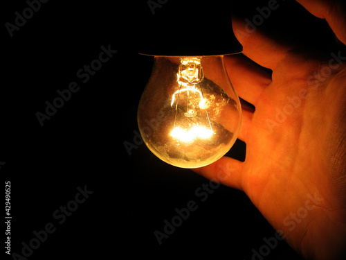 A man's hand reaches for an old shining light bulb in the darkness
