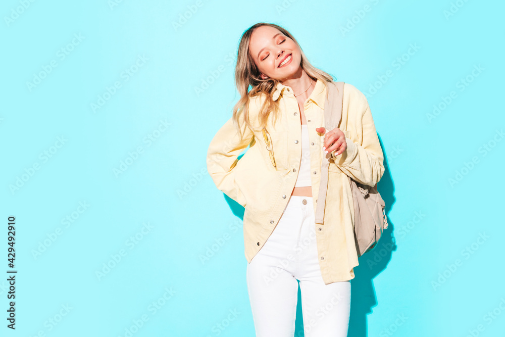 Young beautiful woman looking at camera.Trendy female smiling in casual summer clothes. Positive and funny model posing on grey background in studio with backpack Young beautiful woman looking at camera.Trendy female smiling in casual summer clothes. Positive and funny model posing on grey background in studio with backpack