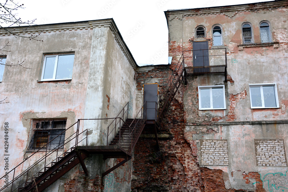 Old staircase and house. An old industrial building with a rusty metal staircase. Collapsed stone structure.