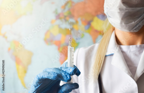 A syringe with a vaccine in the hands of a doctor in protective gloves against the background of a political map. The concept of healthcare and medicine in international politics.