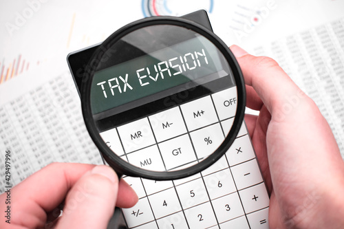 The word tax evasion is written on the calculator. Business man holding a calculator in his hand.
