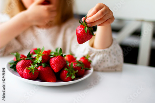 Cute little girl eating fresh strawberry in the kitchen. Healthy vitamin snack for kids. Ripe fresh berries. Harvest season. Natural vitamins .