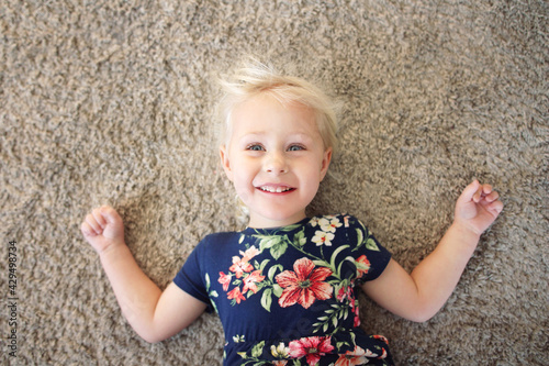Sweet Little Girl Child in Flower Dress Laying on Carpet, Smilin © Christin Lola