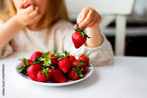 Cute little girl eating fresh strawberry in the kitchen. Healthy vitamin snack for kids. Ripe fresh berries. Harvest season. Natural vitamins .