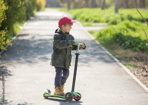 a beautiful boy rides a three-wheeled scooter on the sidewalk. Spring green background