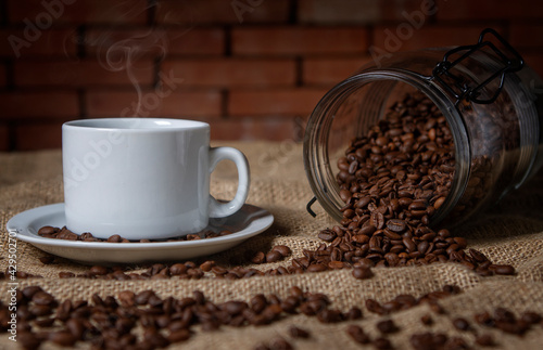 cup of coffee and a glass jar with coffee beans scattered on the table.