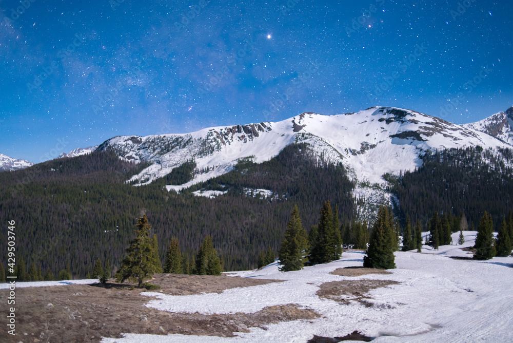 The Milky Way peaking out over a snow capped mountain on a beautiful moonlit night