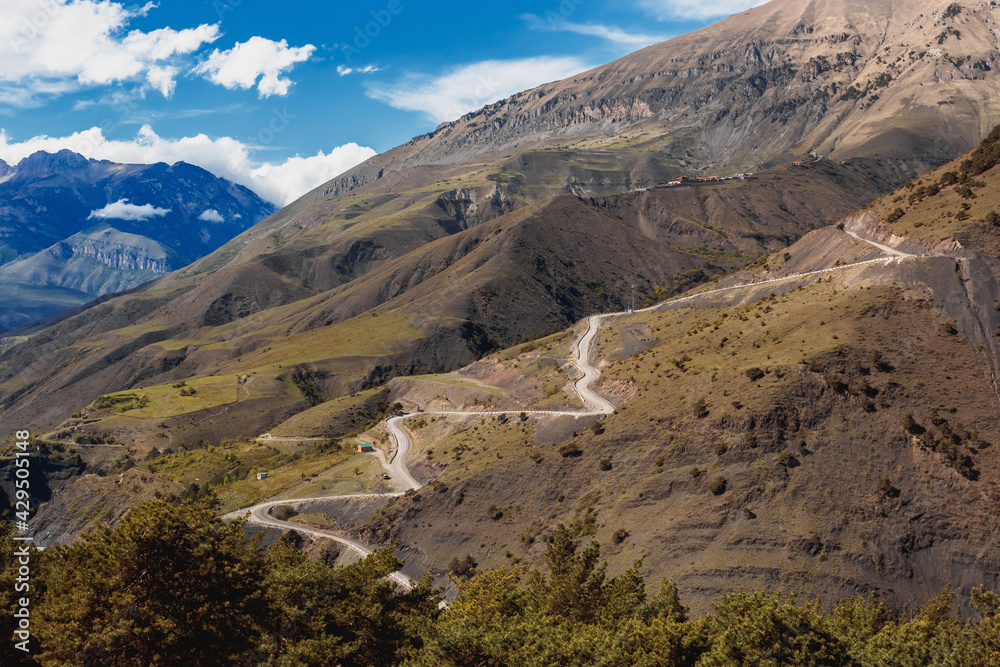 Obraz premium Panoramic view of Table Mountain in Ingushetia, Russia. Mountain serpentine road. Landscape, rocks and blue sky. The road to the top. Mountain climbing. Tourist adventure.