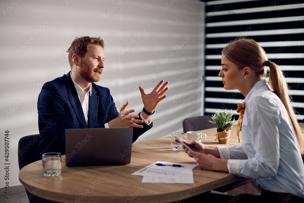 Obraz premium Businessman talking to female coworker while using laptop during a meeting in the office.