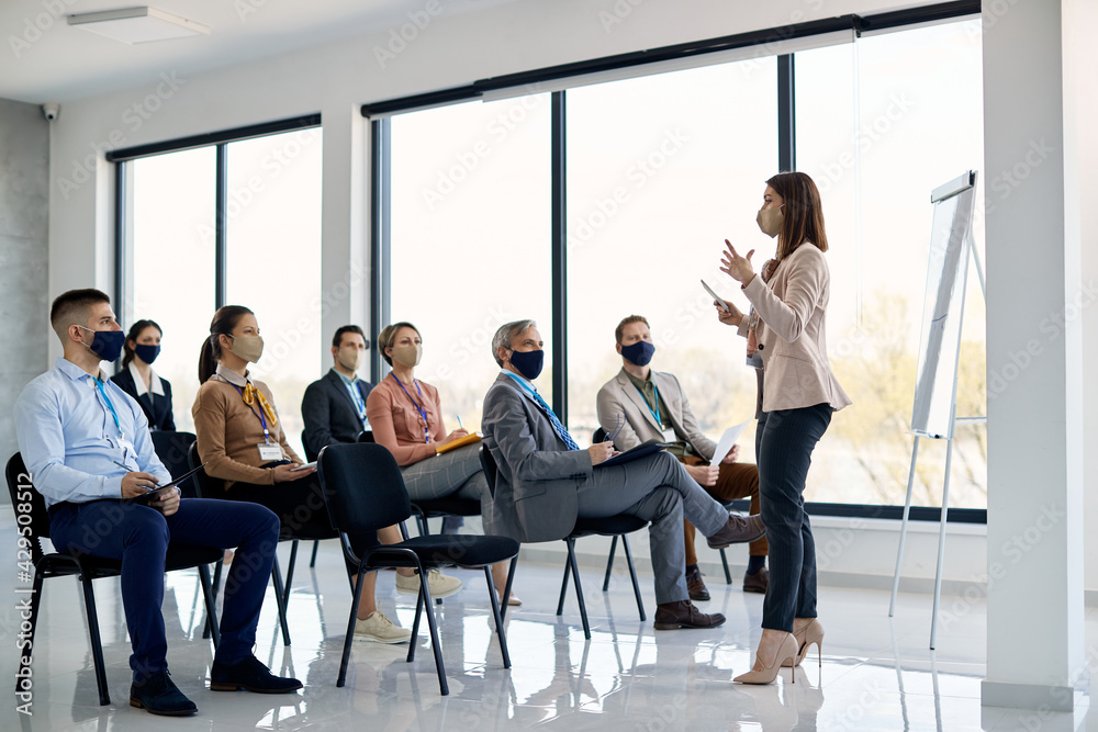 Businesswoman giving presentation to group of her co-workers in board room during coronavirus pandemic.