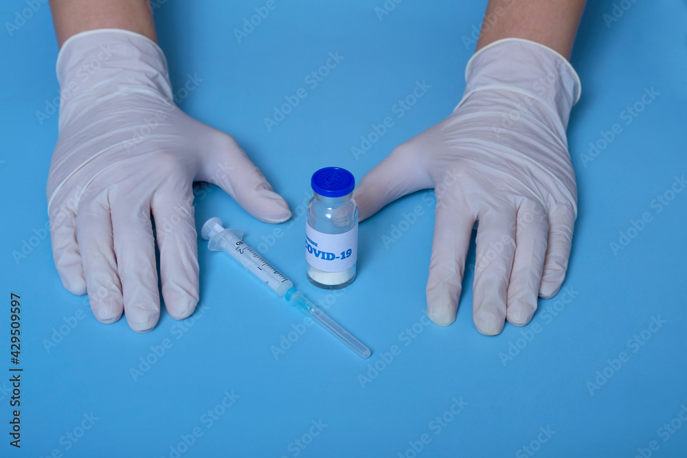 Fototapeta premium Medical concept. On a blue background doctor's hands in white gloves, coronavirus vaccine, syringe. virus protection.Concept: prevention of coronavirus