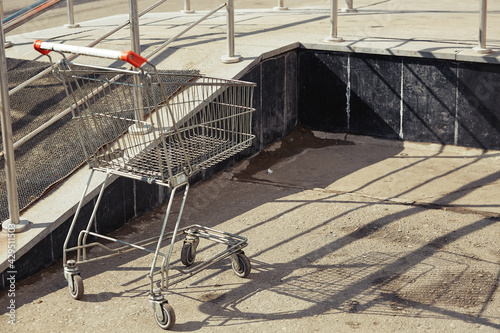 An empty supermarket shopping cart from a hypermarket is abandoned on the street.
