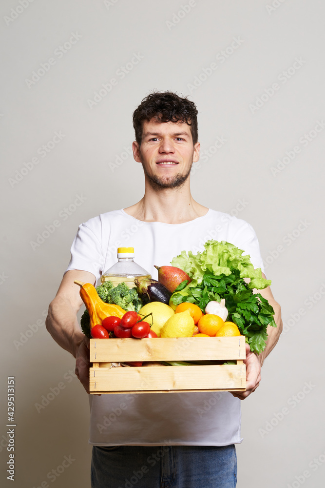 online shopping concept. A man in T-shirt holds a box of fresh food in his hands. Food delivery from the supermarket, from farmers. Delivery during quarantine online shopping concept. A man in T-shirt holds a box of fresh food in his hands. Food delivery from the supermarket, from farmers. Delivery during quarantine