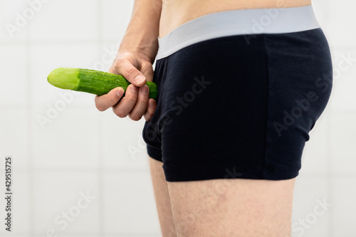 symbol of a male penis hold by hand in front of shorts to visualize average phallus without foreskin while masturbation and as visualization for circumcision photo