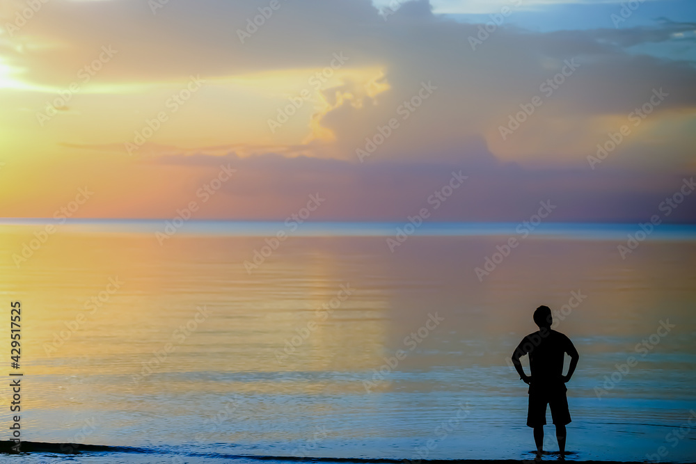 Silhouette Man standing on the beach with sunset background.