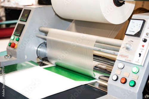 The industrial laminator applies the film to the paper in the production room of the printing house photo