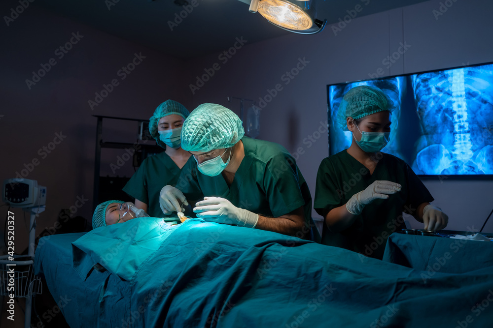 Group of surgeons working and examining the operation in operating room with surgery equipment.