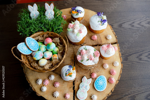 Christian Easter 2021. Easter decor-cakes decorated with meringue and flowers, painted eggs in a basket on a natural wooden background.
