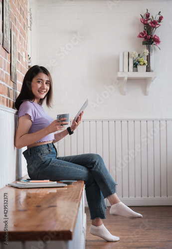 Smiling young asian woman entrepreneur checking order by digital tablet while sitting at her home office. Work From Home concept.