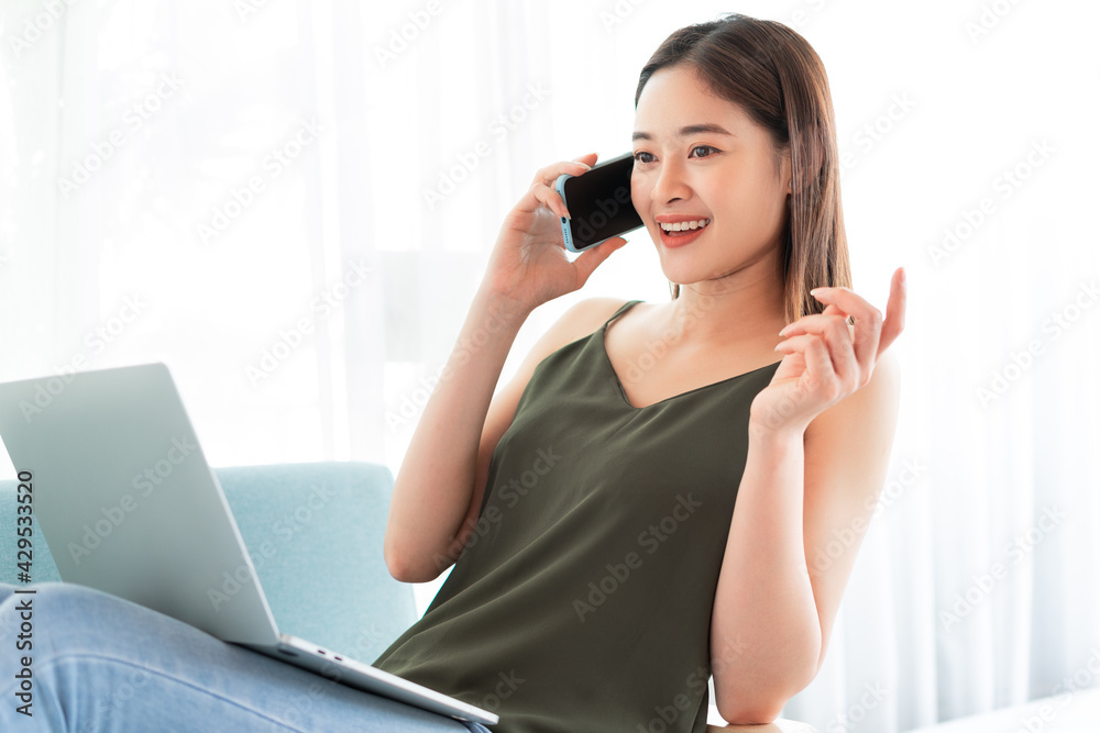 Asian woman talking on the phone while using laptop Asian woman talking on the phone while using laptop