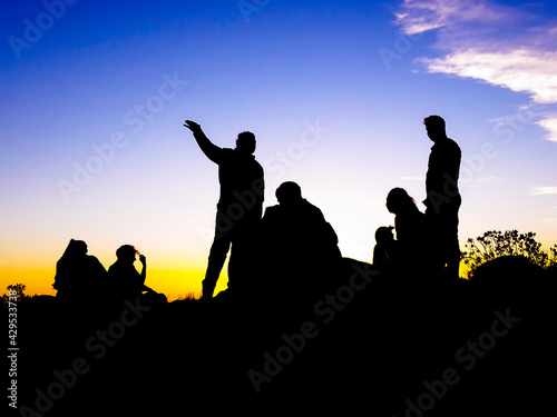 Siluetas humanas con alto contraste, observando el atardecer en la cima del cerro Uritorco, capilla del monte, córdoba, argentina. Guía turístico explicando el paisaje al grupo de viaje.