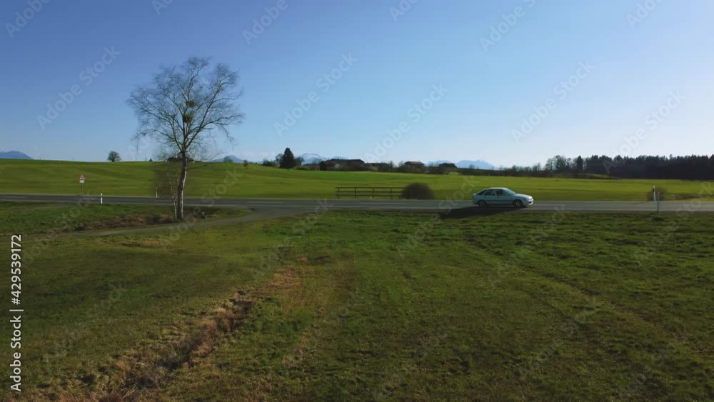 Scenic 4K aerial view upon a small street in spring with cars driving at Bavaria's famous lake Chiemsee in the rural countryside with a beautiful blue sky and the alps mountains in the background Scenic 4K aerial view upon a small street in spring with cars driving at Bavaria's famous lake Chiemsee in the rural countryside with a beautiful blue sky and the alps mountains in the background