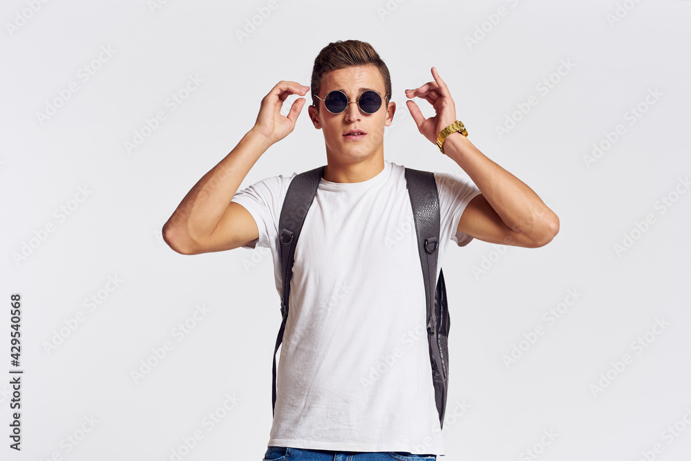 Fototapeta premium man in sunglasses with a backpack on his back and in a white t-shirt on a light background cropped view of emotion