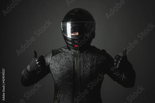 A happy motorbiker in helmet is showing a thumbs up gesture on a dark background. © Dmitriy