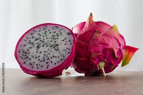 Dragon fruit sliced into 2 pieces with one piece facing back on a wooden table. photo