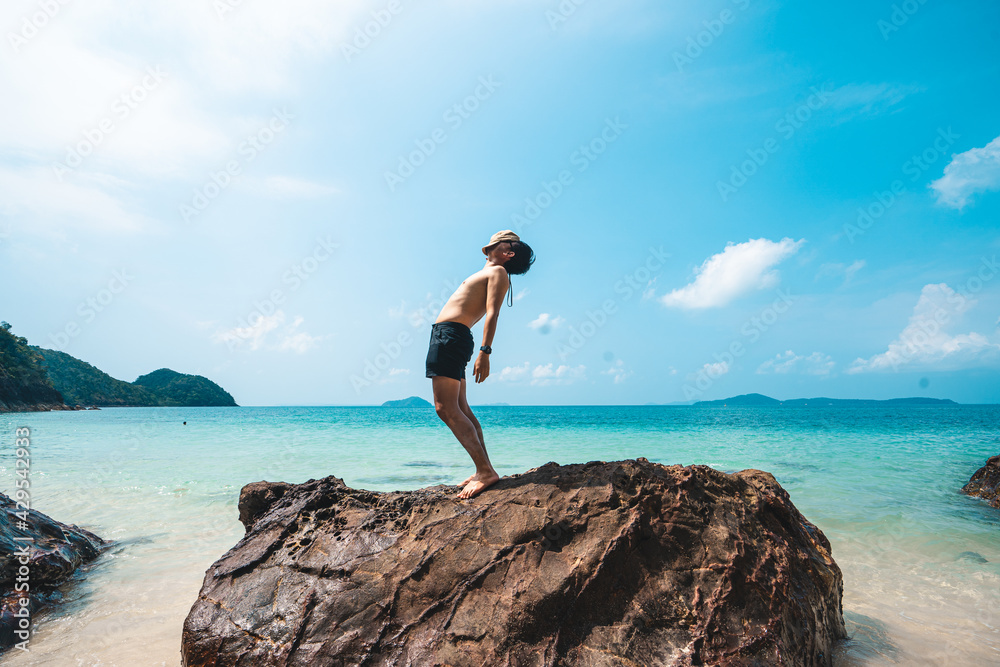 A man standing on a rock at the beach in summer