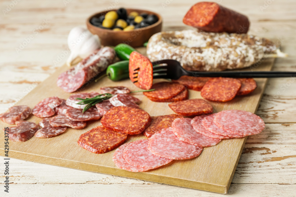 Board with slices of different sausages on wooden background