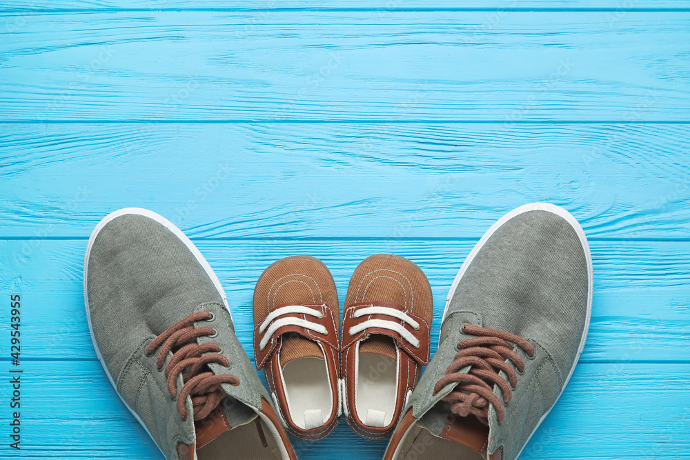 Naklejka premium Parent and child shoes on blue wooden background, family concept with adult sneakers and baby footwear, top view with copy space