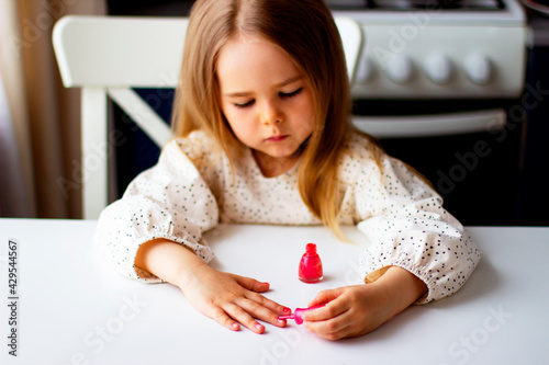 Little girl paints her nails with pink nail polish. Cute toddler girl  playing with colorful nail polish doing manicure. Cosmetics and beauty concept.