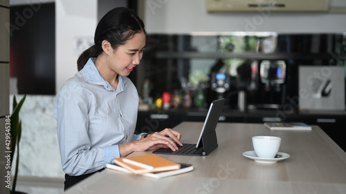 Businesswoman smiling working online with computer  tablet at home kitchen counter.