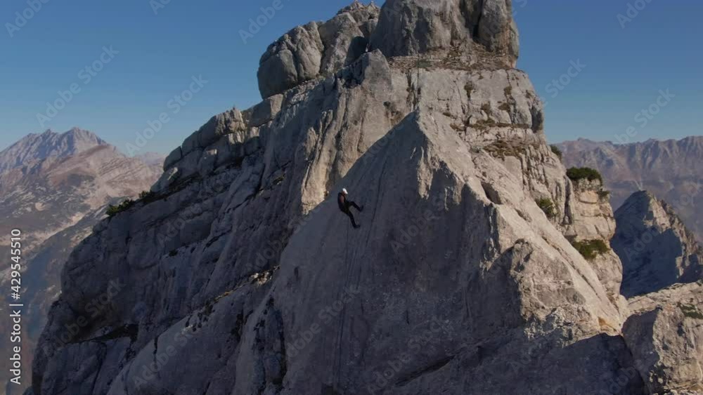 An aerial drone shot of a man abseiling down a steep cliff face high up in a vast mountain range - daytime. An aerial drone shot of a man abseiling down a steep cliff face high up in a vast mountain range - daytime.