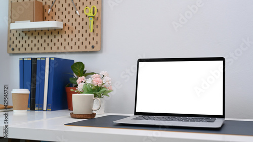 Close up view of mock up computer laptop with blank screen and office supplies on white desk in home office.