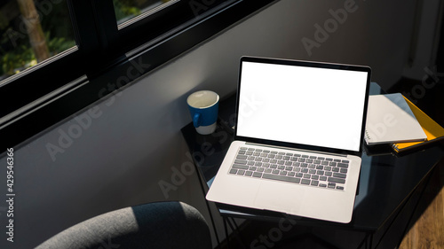 Mock up computer laptop with blank screen, paperwork and coffee cup on black table in office.