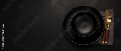 Table setting with a black plates on a black background. Minimalism concept.