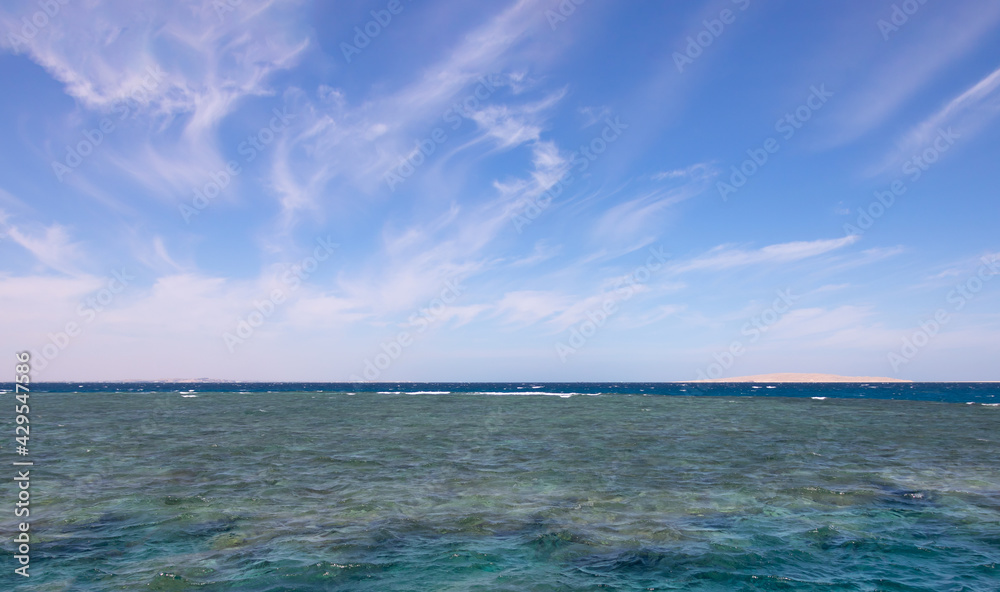 Panoramic view of a coral reef in the Red Sea, the horizon line separates the clear turquoise water and the blue sky with white feather clouds
