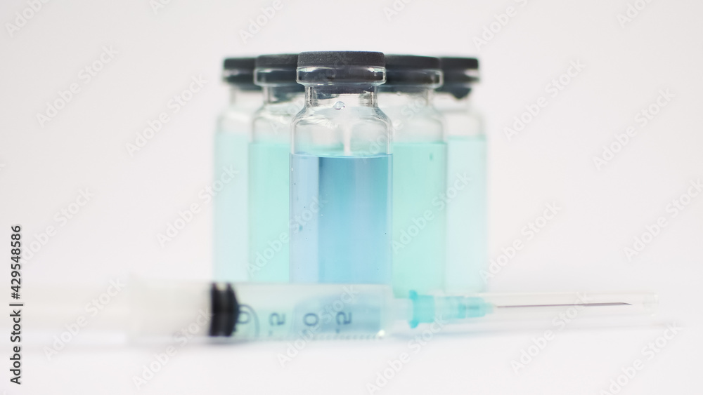 Vial vaccine, glass ampoules with transparent and blue liquid, a syringe is lying near on white background, global vaccination concept Vial vaccine, glass ampoules with transparent and blue liquid, a syringe is lying near on white background, global vaccination concept