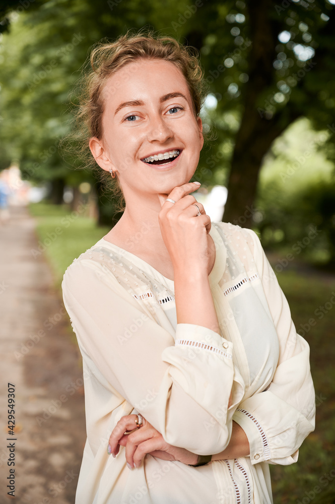 Waist up of young woman smiling while demonstrating results of dental braces treatment. Joyful female with orthodontic brackets on teeth standing on the street. Concept of dentistry. Waist up of young woman smiling while demonstrating results of dental braces treatment. Joyful female with orthodontic brackets on teeth standing on the street. Concept of dentistry.