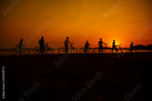 Silhouette of children standing by bicycle on the beach with beautiful sunset nature. Concept. friendly family.flare light.selected focus.group  children  team  bicycle.