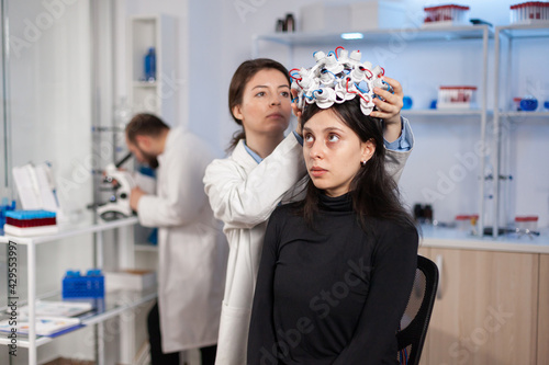 Woman wearing brain wave headset in modern medicine lab with neurologist doctor health physician. Neuroscience medic putting sensors on patient. Finding cure for disease.