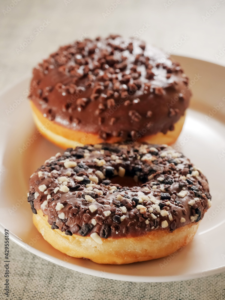 Doughnut with chocolate icing on a white plate. Pastry product. Delicious and unhealthy choice of desert
