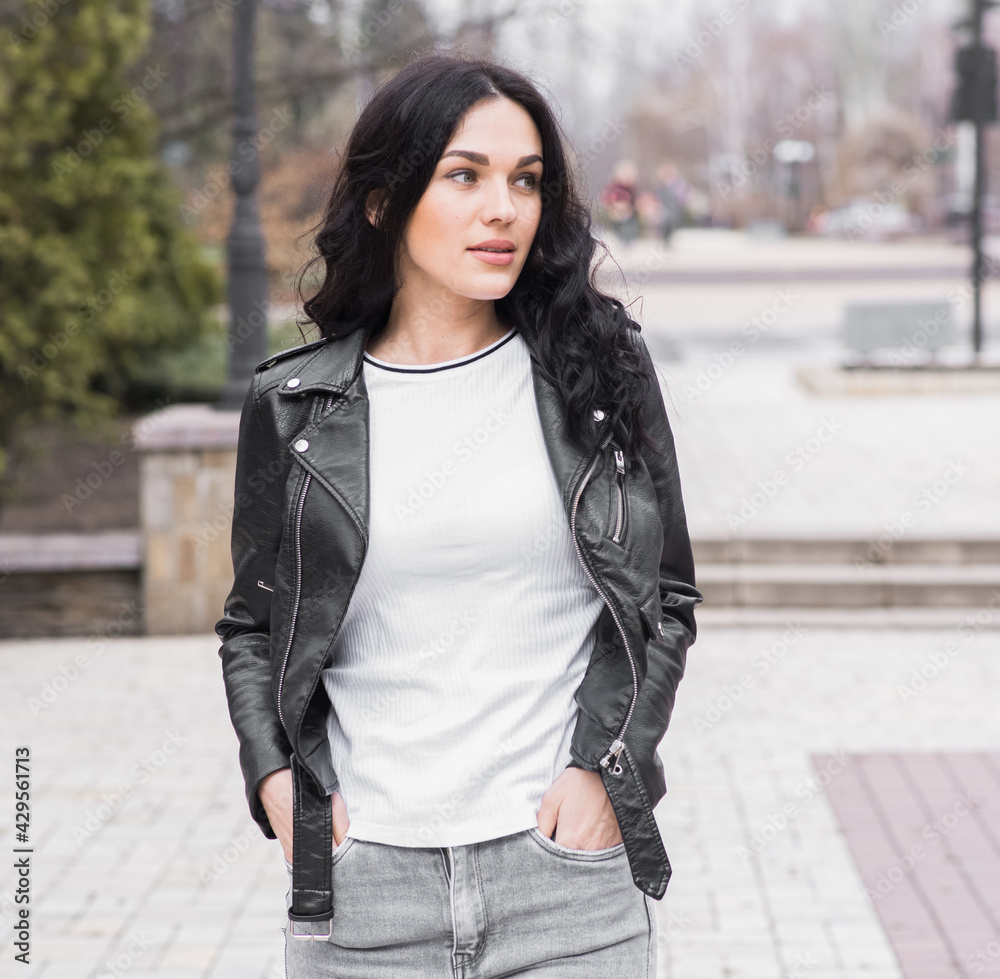 Fototapeta premium Beautiful brunette woman with curly hair posing on the street while walking