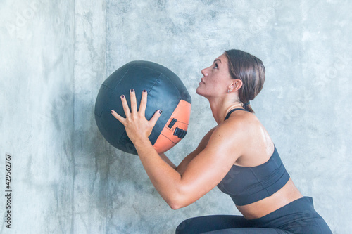 A beautiful female athlete throws a medicine ball at the wall during training at a gym